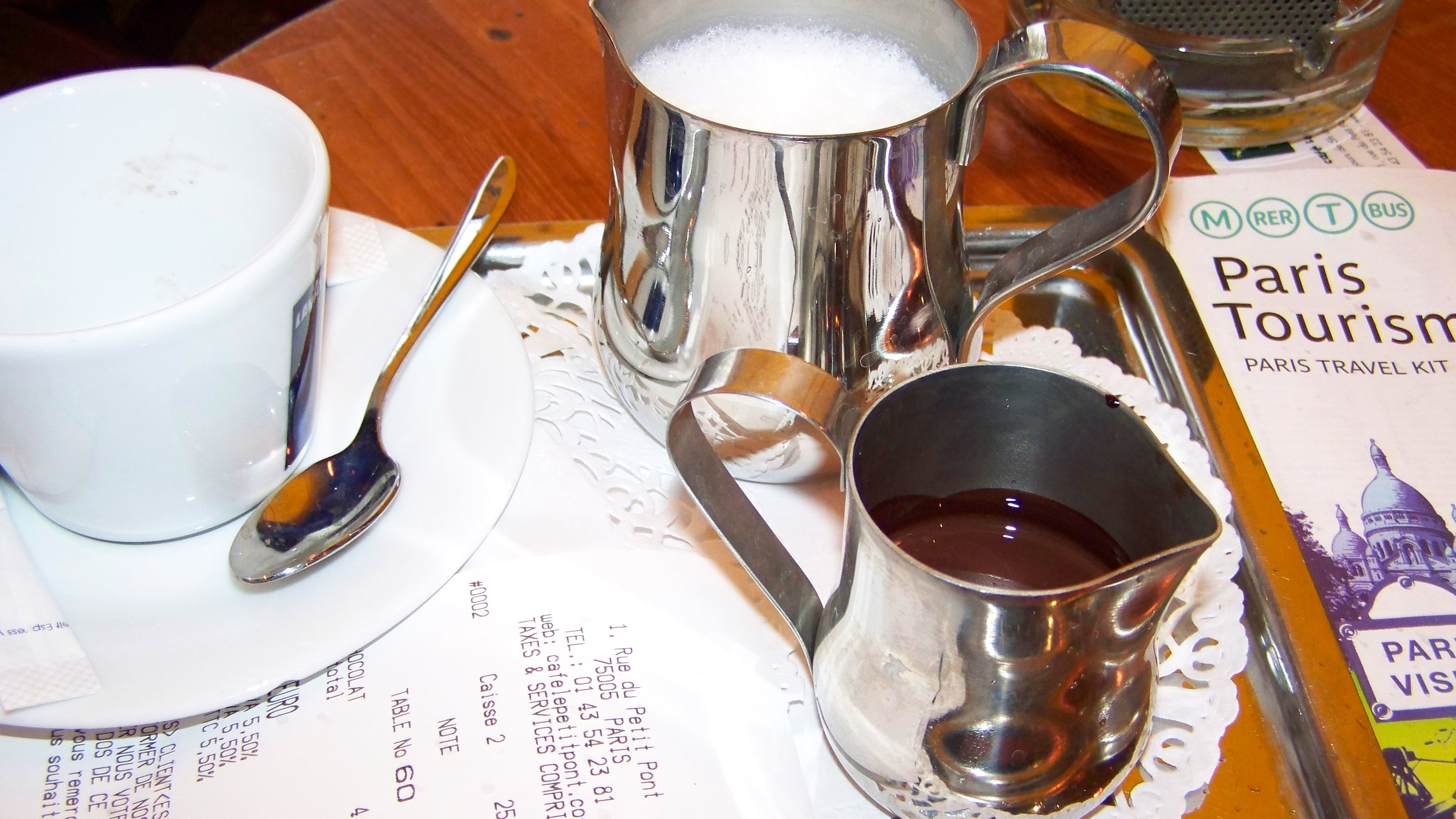 Hot chocolate with silver pitchers, Paris bill and Paris Tourism guide at a Paris cafe